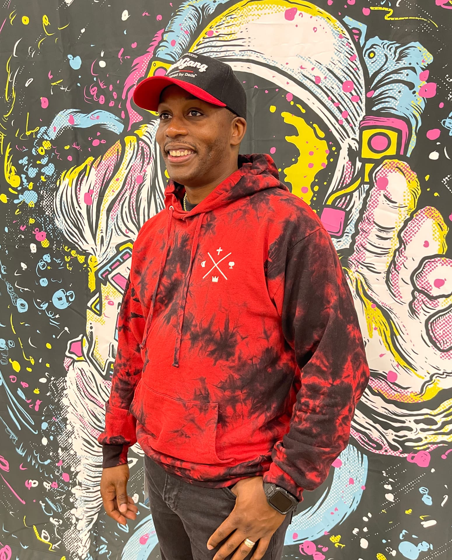 Man wearing a red custom tie-dye hoodie in front of a mural by Hardiewear