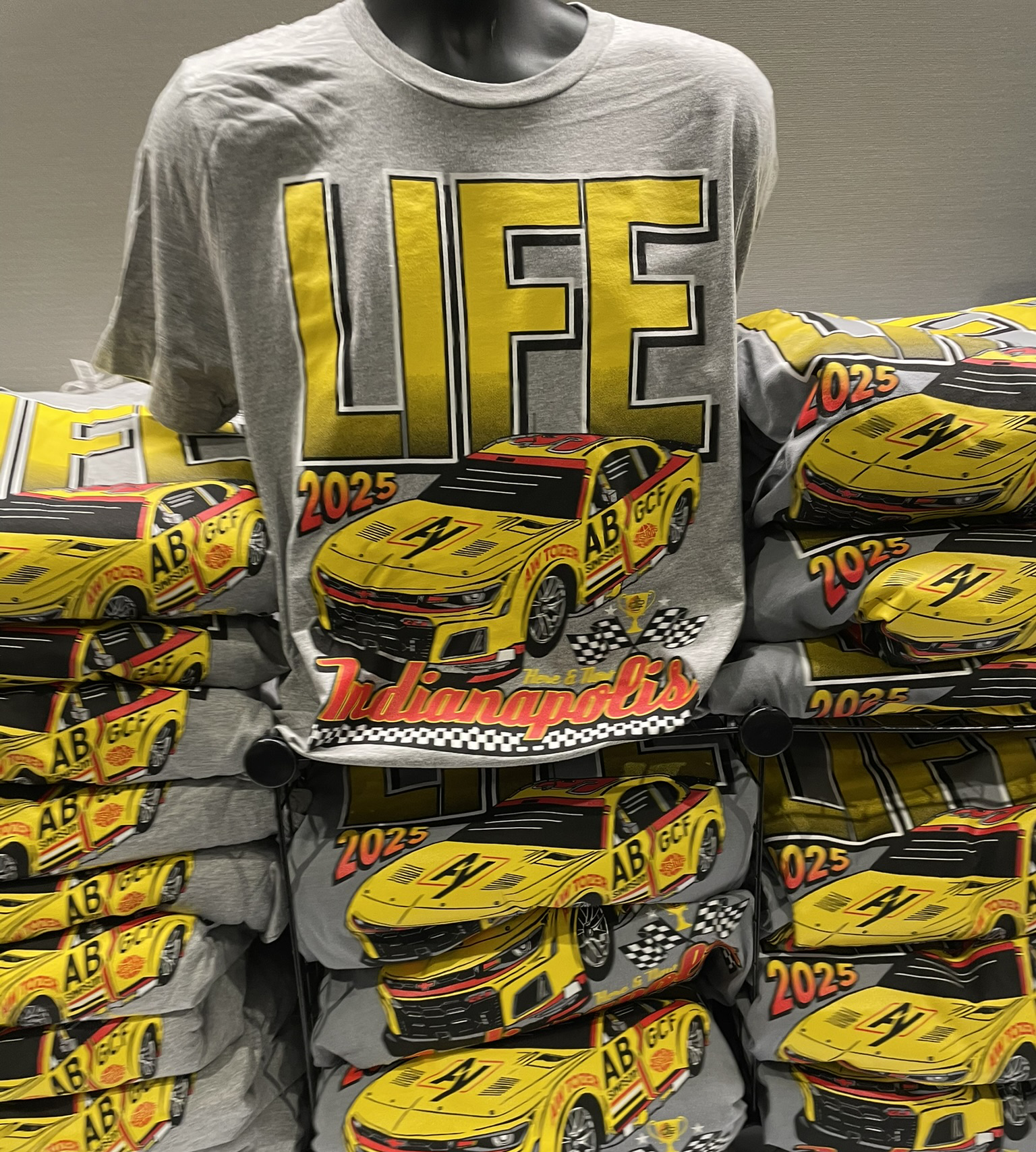 Custom screen-printed racing tees with a yellow stock car graphic stacked on display by Hardiewear