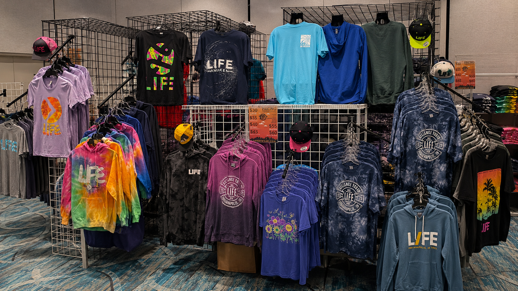 Event merch booth with custom tie-dye hoodies, printed tees, and embroidered hats on display racks by Hardiewear
